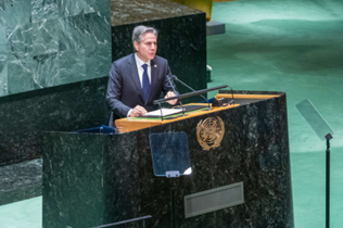 Secretary of State Antony J. Blinken stands in a dark suit at a large podium in the United Nations in New York City