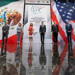 Secretary Blinken stands on a stage with five other officials in front of flags of the United States and Mexico.