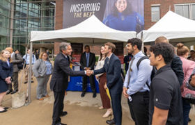 Participants watch as Secretary Blinken, who is wearing a dark colored suit, shakes hands with a male student. 