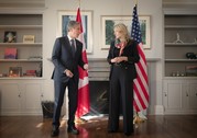 Secretary Blinken and Canadian Foreign Minister Joly stand and talk in a room in front of a fireplace and the U.S. and Canadian flags.