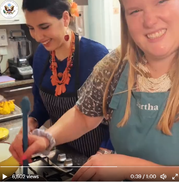 Screenshot of video with two embassy staff members wearing aprons cooking a special meal. 