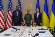 Secretary Blinken, Ukrainian President Zelenskyy, and Secretary of Defense standing side by side with the U.S. and Ukrainian flags behind them. 