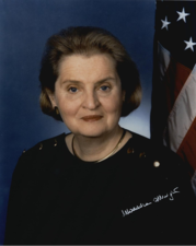 Official photograph of Secretary of State Madeline Albright wearing a black blouse in front of the U.S. flag. 