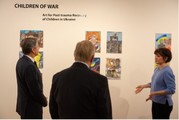 Secretary Blinken and two others look at colorful paintings on a white wall. Text on the wall reads: "Children of war"