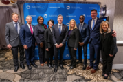 Secretary of State Blinken stands with eight U.S. mayors. Behind them is a blue screen with the logo of the United States Conference of Mayors.