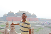 A man in a yellow and black striped shirt posing in front of the Forbidden City while studying abroad in China. 