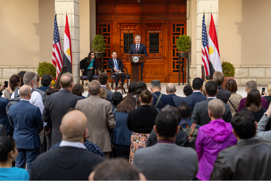 Secretary Blinken speaking to a crowd of people from a podium with a set of U.S. and Egypt flags on each of his side. 
