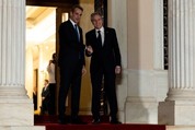 Secretary Blinken and Greek Prime Minister Mitsotakis smile and shake hands in a doorway with large columns flanking them.