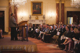 Ambassador Ruth A. Davis speaking at a podium in a ceremony in the State Department’s Benjamin Franklin Room in front of an audience. 