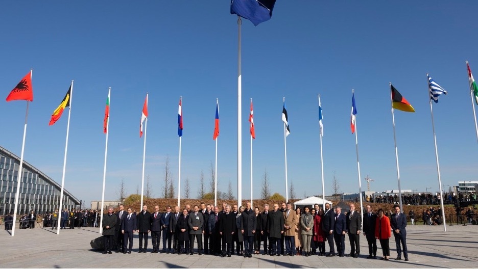 The foreign ministers and representatives of the 31 NATO member nations stand outside under a blue sky. 