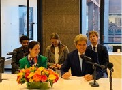 Assistant Secretary Medina sits next to Special Envoy Kerry at a table with a white tablecloth. They are smiling. 