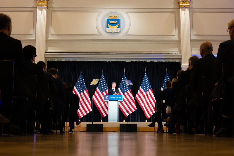 Secretary Blinken giving a speech at podium in front of a seated crowd with U.S. flags behind him.