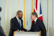 Secretary Blinken and UK Foreign Secretary Cleverly shake hands in front of a podium. A UK flag is behind them. 