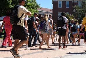 Students wearing backpacks walk outside on a college campus.