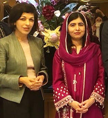 Rina Amiri, in a green blazer, stands next to Malala who is wearing red clothing with embellishments.