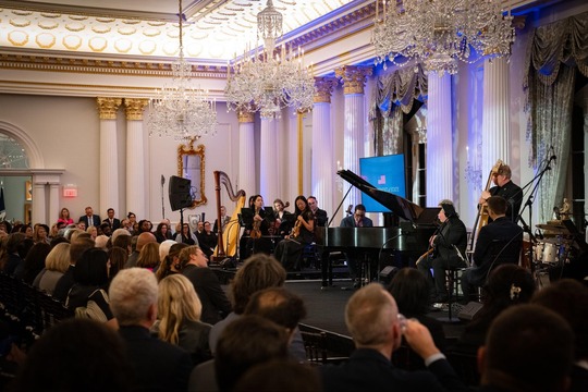 Photo of musicians on stage with their instruments and a crowd sitting in chairs in front of the stage. 
