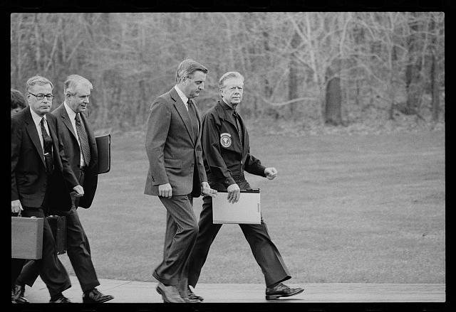 President Carter and his national security team walking past woods while holding folders and briefcases (Public domain)