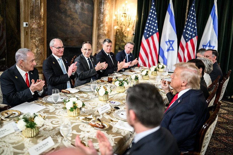 President Trump and Prime Minister Netanyahu at a table at the Mar-a-Lago Club. The Prime Minister and others at the table are applauding.