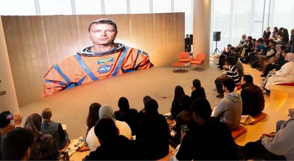People sitting around a television screen showing an astronaut.