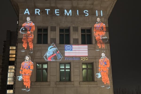 Three American astronauts and one Canadian astronaut are projected on a facade with icons marking Artemis II and America’s Freedom 250.