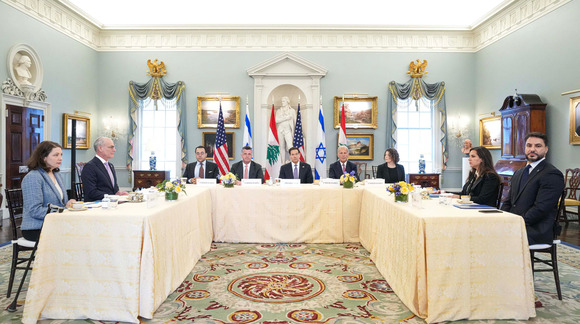 Officials are shown seated at a U-shaped table in a ceremonial room, with the flags of Israel, Lebanon, and the U.S. in the background
