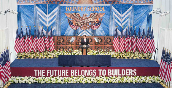 Secretary Rubio speaks from behind a lectern on a stage. Over him is an insignia with an eagle and “FOUNDRY SCHOOL – PROMISES KEPT.”