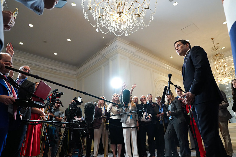 Secretary Rubio stands behind a microphone, facing a large gathering of reporters and videographers.
