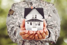 man in military uniform holding model house