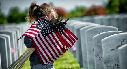 child carrying small american flags through veterans cemetery