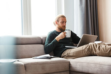 man sitting on couch with laptop and coffee