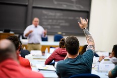 man in classroom with his hand raised