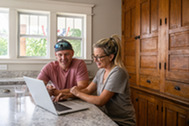 man and woman using laptop while sitting at kitchen counter