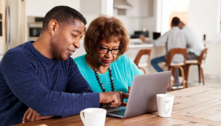 man assisting older woman while looking at laptop together