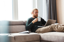 man sipping coffee next to window while on laptop