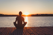 woman in yoga seated position on a pier with the sun setting in the distance