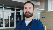 Man in hospital scrubs and wearing a stethoscope smiling.