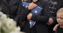 Military funeral with a woman holding a folded American flag.