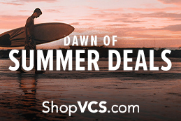 Man with a surfboard on a beach. Dawn of summer deals on shop vcs.