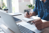 Person on a laptop writing notes while taking an online course.