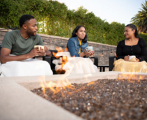 Three people sitting around a fire pit drinking coffee.