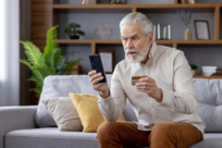 Man with shocked expression looking at smart phone while holding a credit card.