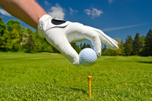 Gloved hand placing golf ball on tee.