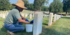 Woman cleaning a headstone at a national Veteran's cemetery.