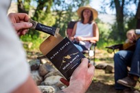 Person holding a small pouch of instant coffee at a campsite.