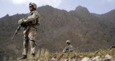 Soldier in uniform standing atop a mountainside in Afghanistan.