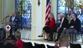 Three people seated on stage and one person standing at a podium at the Buddy Check Summit. 