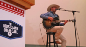 Man in cowboy hat singing and playing guitar.