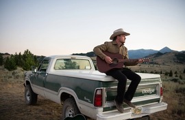 Cowboy sitting on the back of a pickup truck.