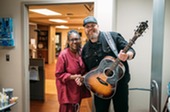 Woman shaking hands with a country music artist holding a guitar.