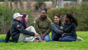 Five people sitting on the grass talking